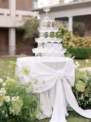 Cocktail hour tower with glasses on a white tablecloth in a garden setting