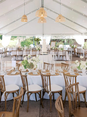 Decorated wedding reception with tables, chairs, and floral arrangements under a white tent.