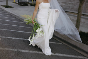 Bride in a white wedding dress holding Lily Boueuet on a sidewalk