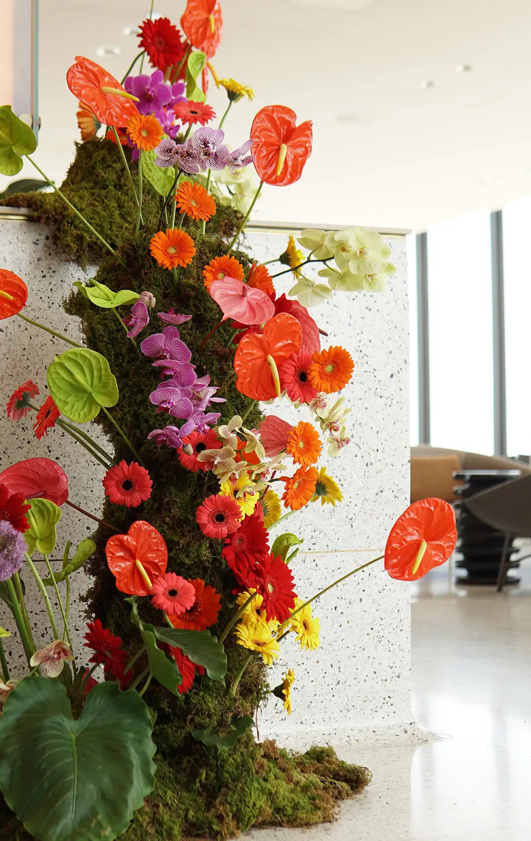 Colorful floral arrangement with red, orange, and purple flowers on a white wall.