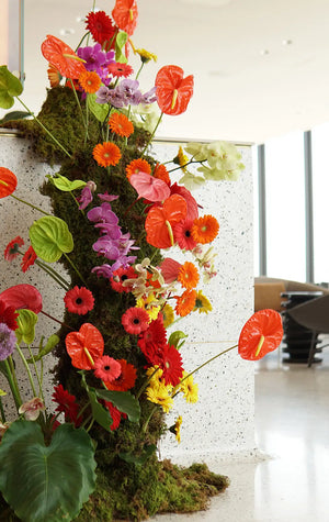 Colorful floral arrangement with red, orange, and purple flowers on a white wall.