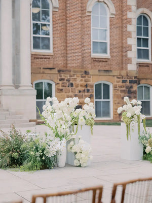 White flowers in vases on a stone surface with a brick building in the background