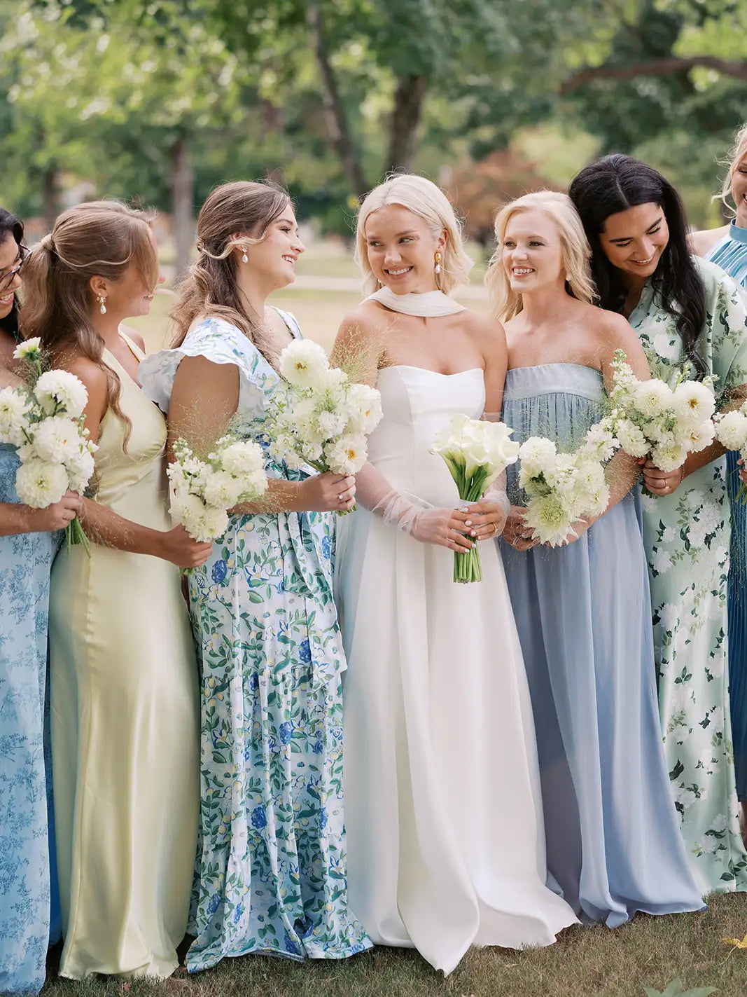 Bride with bridesmaids in pastel dresses holding bouquets outdoors