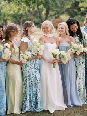 Bride with bridesmaids in pastel dresses holding bouquets outdoors