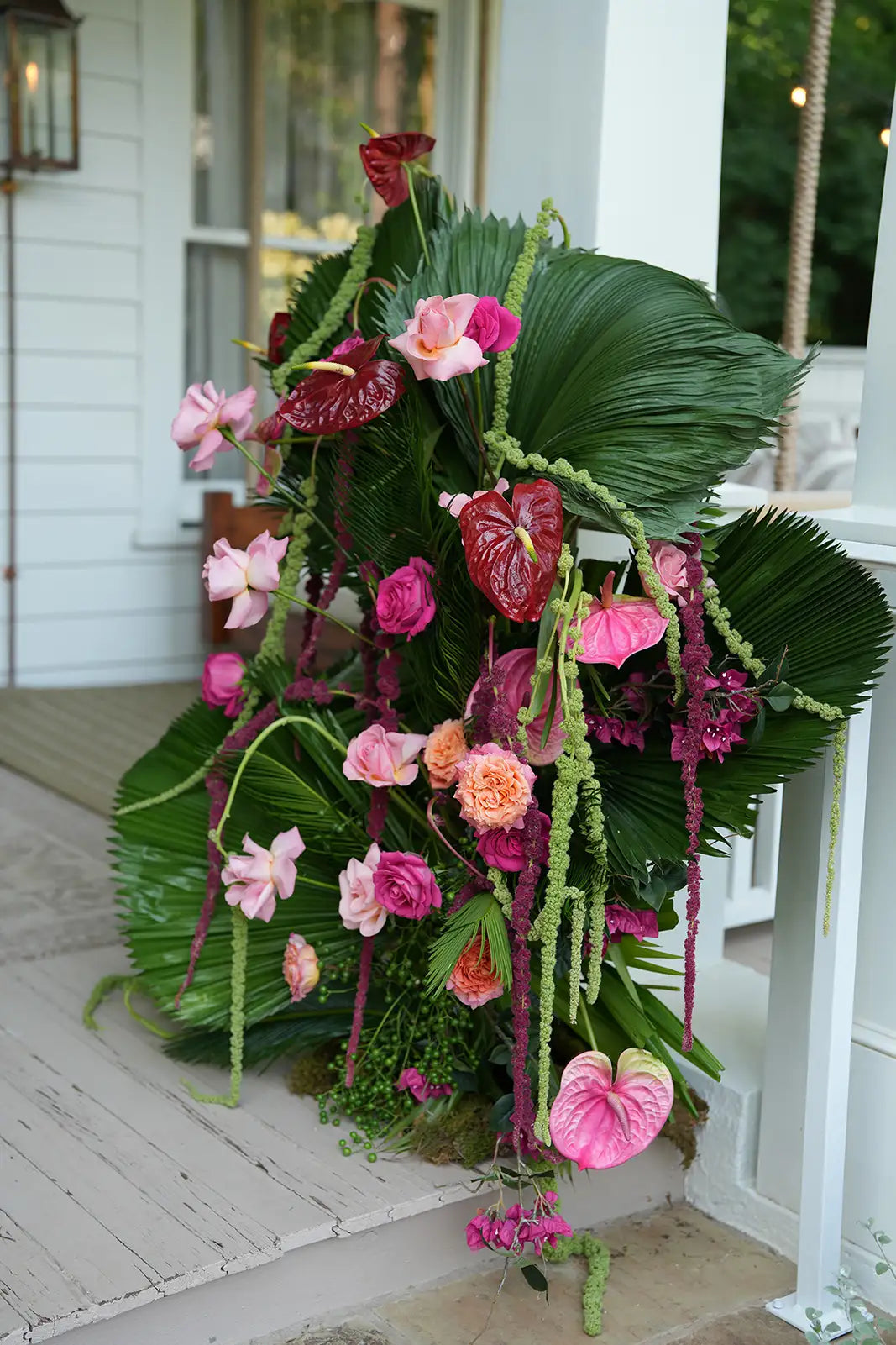 Decorative floral arrangement with pink and red flowers on a porch.
