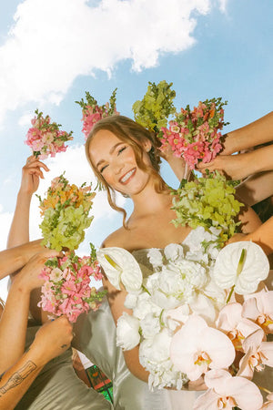 Woman holding a bouquet of flowers with friends against a blue sky.