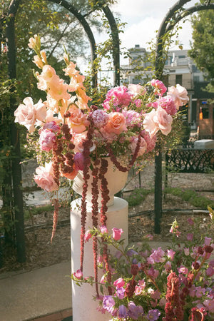 Decorative floral arrangement on a pedestal outdoors with trees and buildings in the background