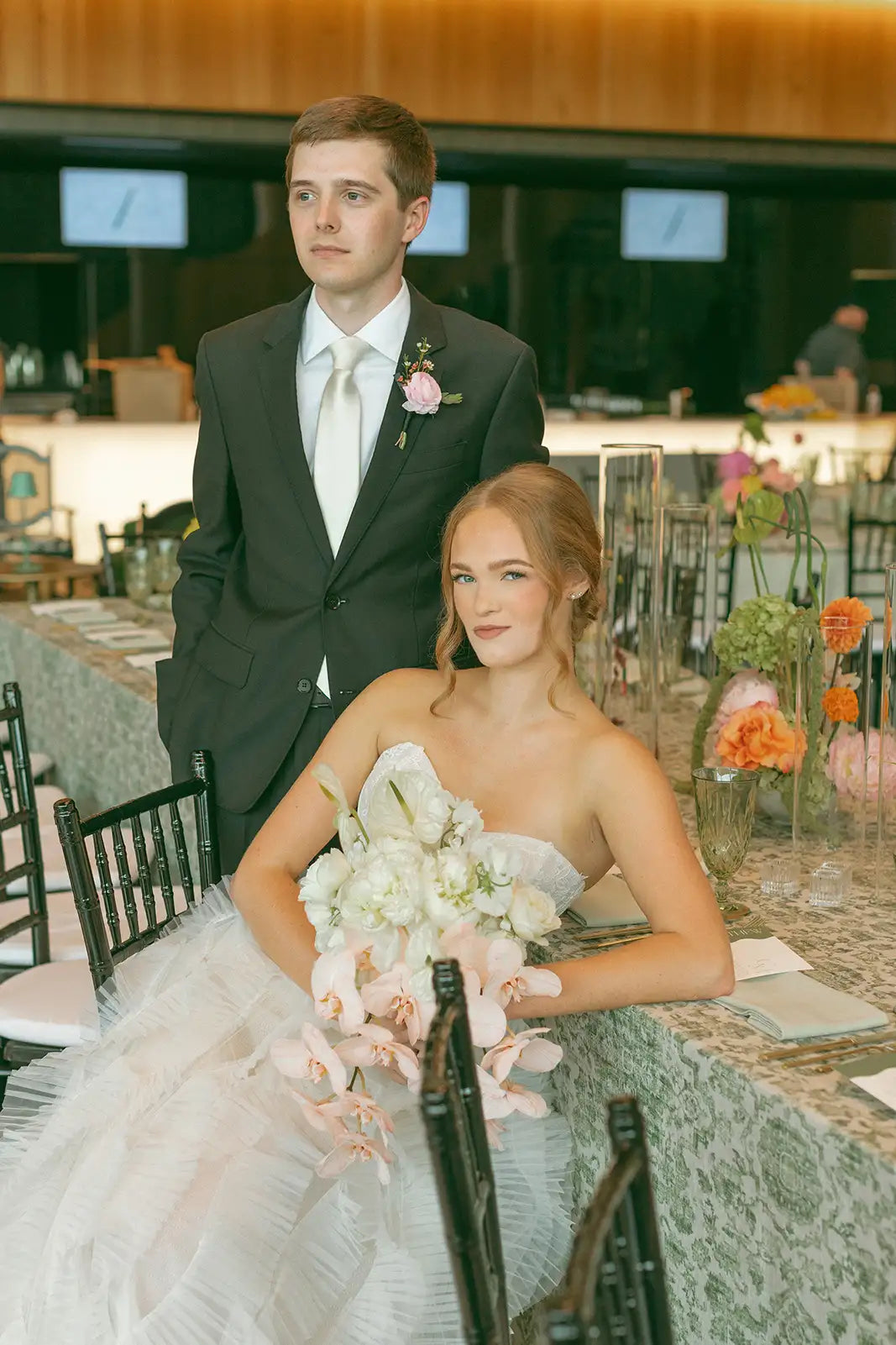 Man and woman in formal attire at a wedding reception with floral decorations.