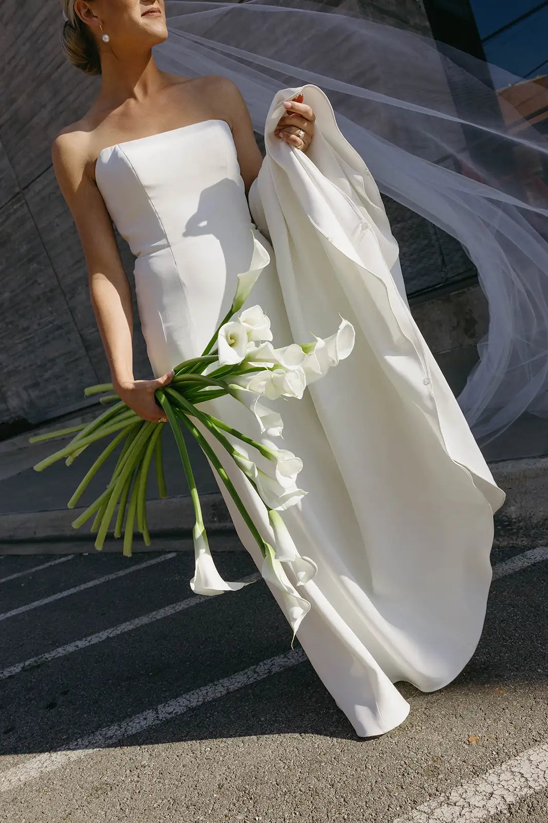Woman in a white wedding dress holding a bouquet of flowers on a street.