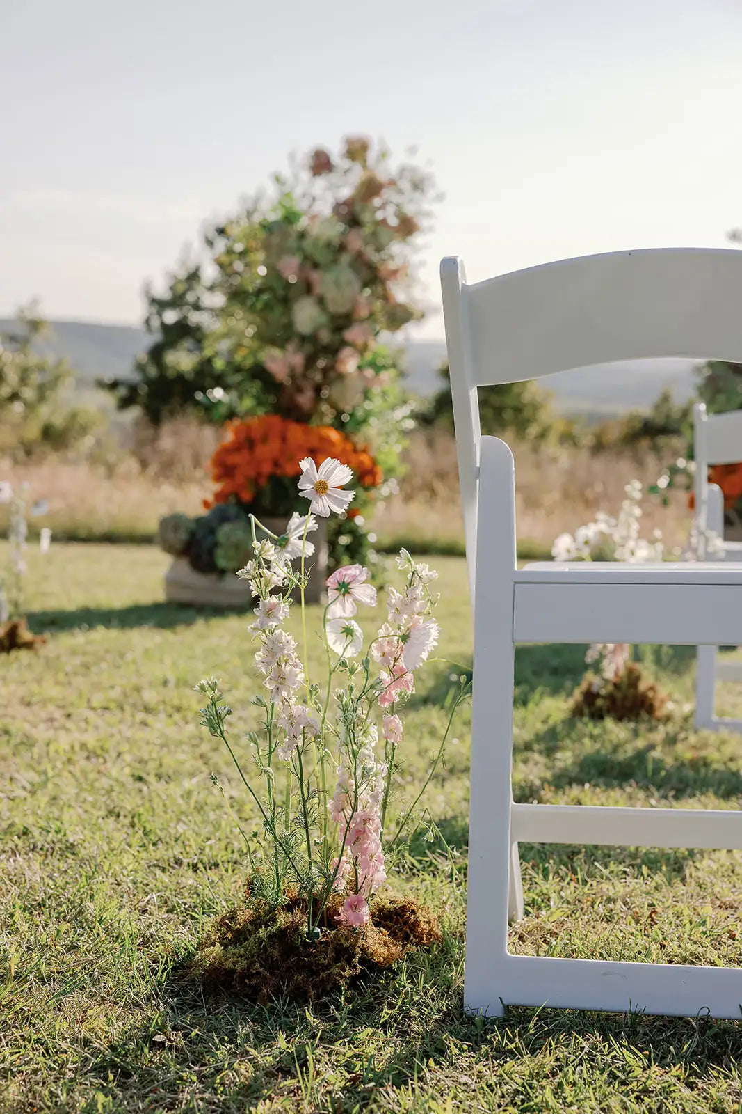 White chair and floral arrangement on a grassy outdoor setting with a floral arch in the background